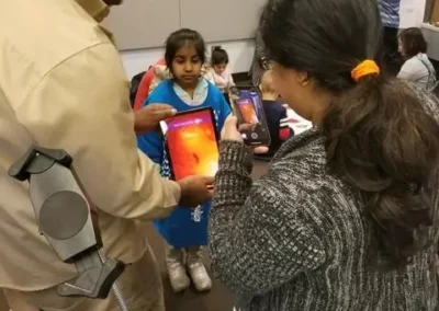 A volunteer shows a girl a thermal-imaging view on a tablet while other children look on at a STEM Night.